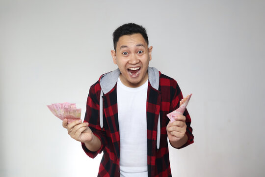 Portrait of happy young Indonesian man holding rupiah money, smiling laughing winning gesture