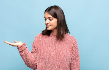 young pretty woman feeling happy and smiling casually, looking to an object or concept held on the...