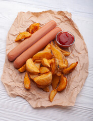 Delicious sausages with fried potatoes and ketchup on a white wooden table