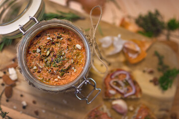 Meat and pepper pate in a glass jar sprinkled with almonds and herbs.