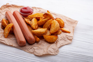 Delicious sausages with fried potatoes and ketchup on a white wooden table