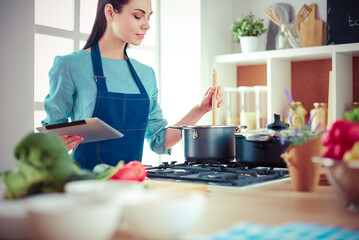 Young woman using a tablet computer to cook in her kitchen