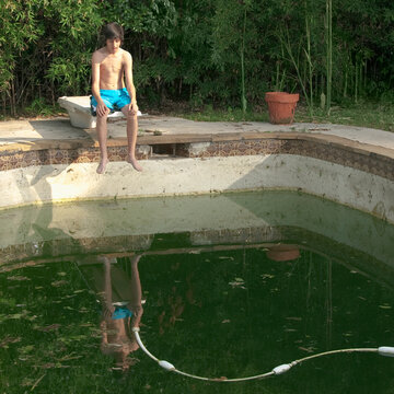 Mixed race teenager looking at dirty swimming pool