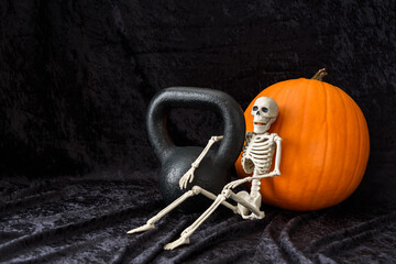 Fall fitness, orange pumpkin, black kettlebell, and white skeleton, on a black velvet background
