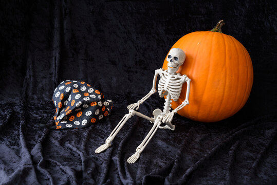 Skeleton, Orange Pumpkin, And A Pumpkin Pattern Face Mask On A Black Velvet Background
