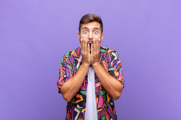 young man feeling shocked and scared, looking terrified with open mouth and hands on cheeks