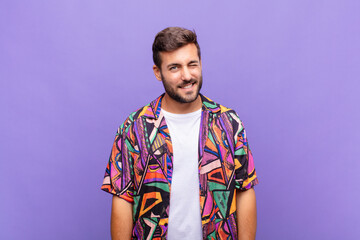 young man looking happy and friendly, smiling and winking an eye at you with a positive attitude