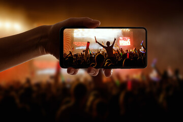 Silhouette of hand using camera phone to take pictures and videos at pop concert, festival