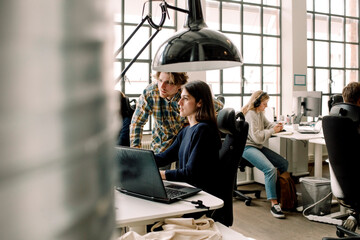 Businessman explaining while coworker looking at computer in office