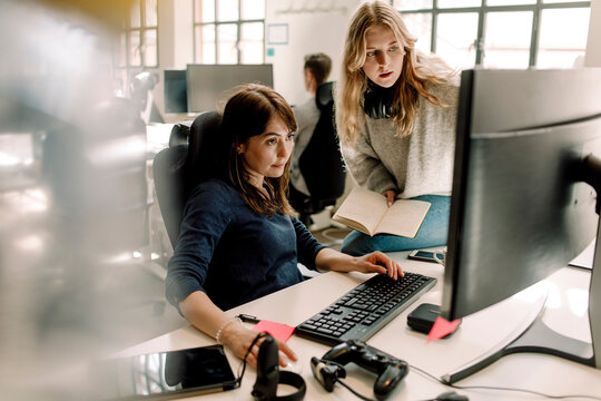 Female colleagues discussing while sitting in office