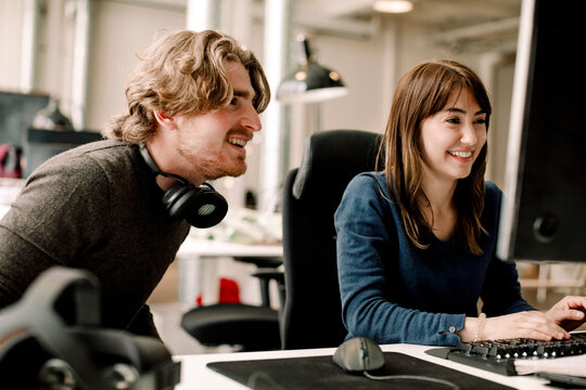 Male and female smiling professionals discussing while sitting in office