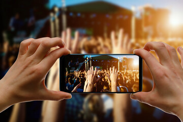 Silhouette of hand using camera phone to take pictures and videos at pop concert, festival