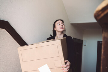 Confident delivery woman with cardboard box looking up against wall