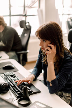 Female entrepreneur working on programming while talking on phone at workplace