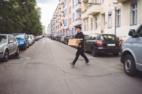 Confident delivery man with cardboard box walking on street in city