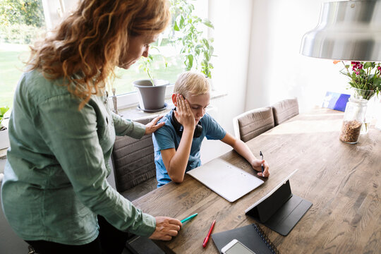 High angle view of mother looking at son studying by table