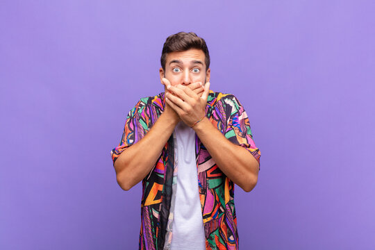 young man covering mouth with hands with a shocked, surprised expression, keeping a secret or saying oops