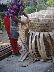 a woman stands beside the basket that is usually used for storing tobacco. the basket is made of bamboo and dried banana stalks
