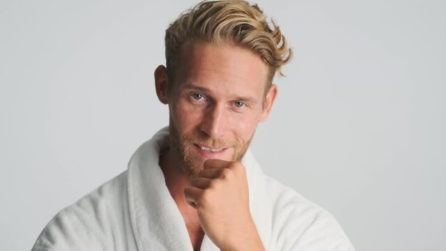 Handsome blond bearded man in bathrobe flirting on camera over white background