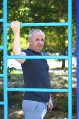Obraz premium Senior man doing exercises in the outdoor gym. The concept of maintaining health at any age. Recovering from a heart attack or stroke. Selective focus. Toning.