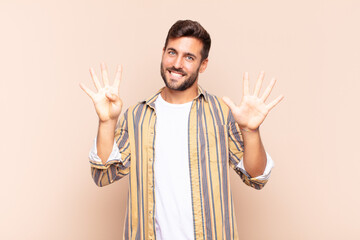 young man smiling and looking friendly, showing number nine or ninth with hand forward, counting...