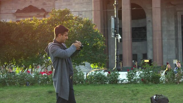 Tourist photographing sights and landmarks. Media. Young traveler man taking pictures on his camera in the city park on the background of huge building with granite pillars.