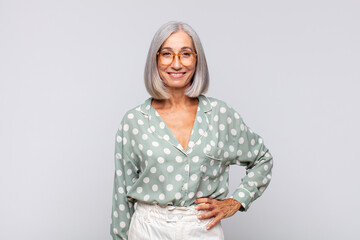 gray haired woman smiling happily with a hand on hip and confident, positive, proud and friendly...