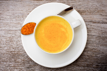 Golden milk ( turmeric latte ) in white ceramic cup with tumeric powder in spoon isolated on rustic wood table background. Top view. Flat lay.