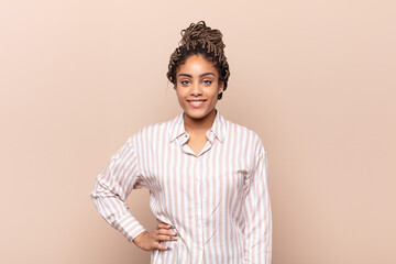 young afro woman smiling happily with a hand on hip and confident, positive, proud and friendly...