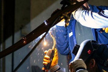 The welder is welding to steel plate material with gas metal arc welding process in the workshop.
