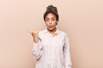 young afro woman looking astonished in disbelief, pointing at object on the side and saying wow,...