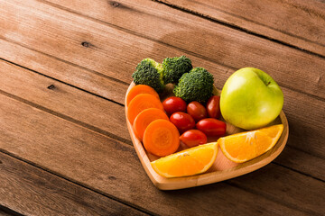 Top view of fresh organic fruits and vegetables in heart plate wood (apple, carrot, tomato, orange, broccoli) on wooden table, Healthy lifestyle diet food concept.