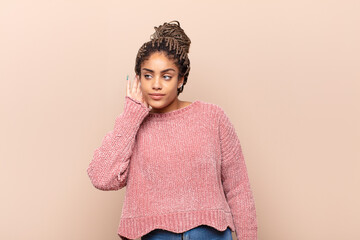 young afro woman looking serious and curious, listening, trying to hear a secret conversation or...