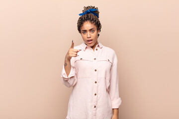 young afro woman pointing at camera with an angry aggressive expression looking like a furious,...