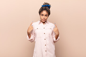 young afro woman with a bad attitude looking proud and aggressive, pointing upwards or making fun...