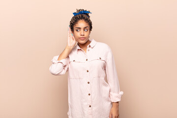 young afro woman looking serious and curious, listening, trying to hear a secret conversation or...