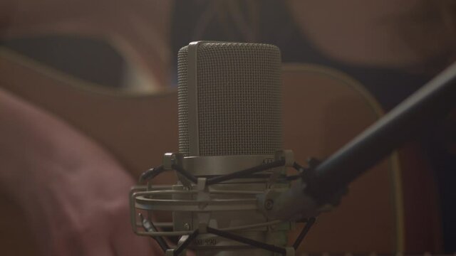 a female hand strums a guitar recording herself on the microphone right in front of her. Close up on the condenser mic 