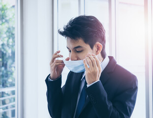 Young Asian businessman in suit wearing medical face mask in office.