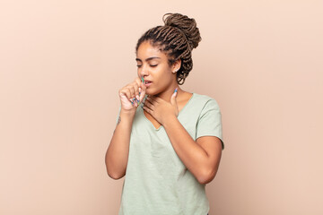 young afro woman feeling ill with a sore throat and flu symptoms, coughing with mouth covered