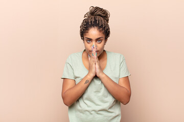 young afro woman feeling worried, hopeful and religious, praying faithfully with palms pressed,...