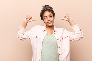 young afro woman feeling proud, arrogant and confident, looking satisfied and successful, pointing...