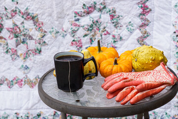 Pumpkin, gourds, gardening gloves, and coffee or tea on a table in front of a quilt with copyspace