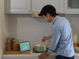 Male cooking and looking recipe on mock up tablet in modern kitchen room