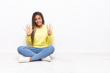 young afro woman smiling and looking friendly, showing number nine or ninth with hand forward,...