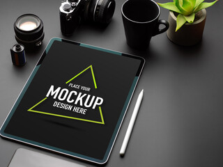 Black table with mock up tablet, camera, mug, plant pot and copy space