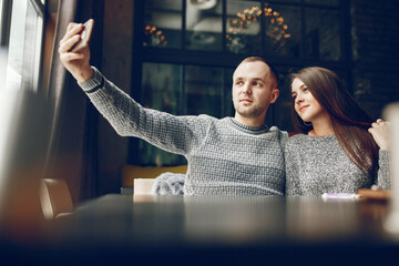 Cute couple sitting in a cafe. Pair in a gray sweaters. Man with mobile phone