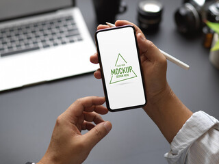 Male hands using mock up smartphone while working with camera and laptop in office