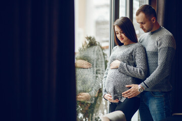 Cute couple standing in a cafe. Pair in a gray sweaters. Pregnant woman standing near window