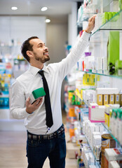 Cheerful male customer looking for right medicine in pharmacy