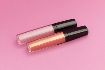 par de brillos labiales rosa y cobre aislados sobre fondo rosa plano cenital